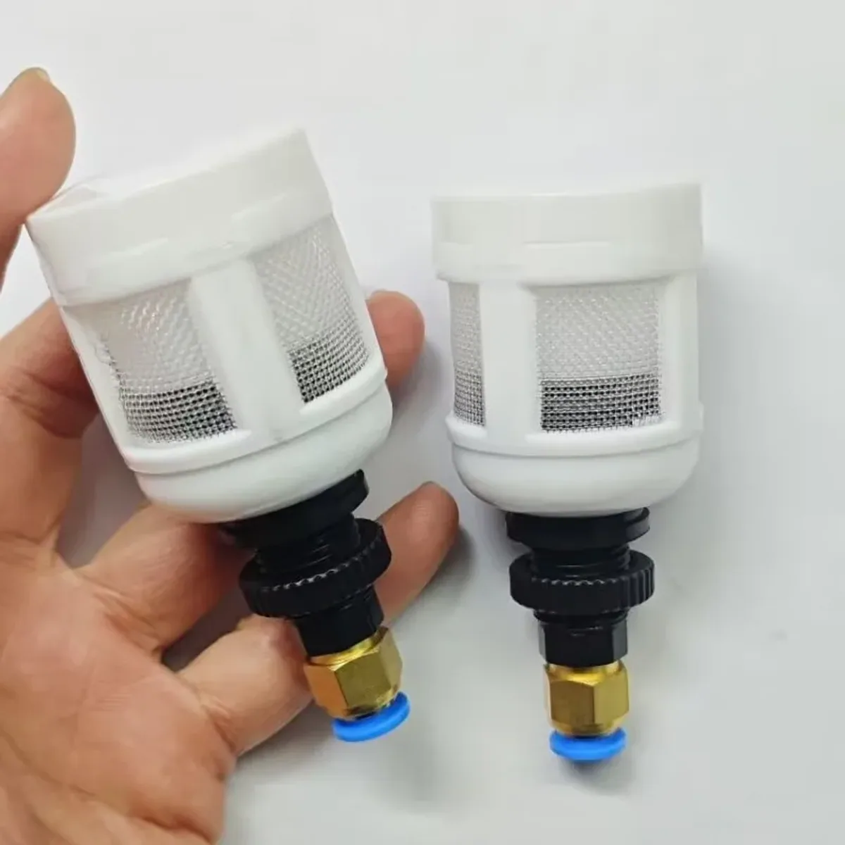 Two white mesh drain valve units with brass fittings, one held in a hand