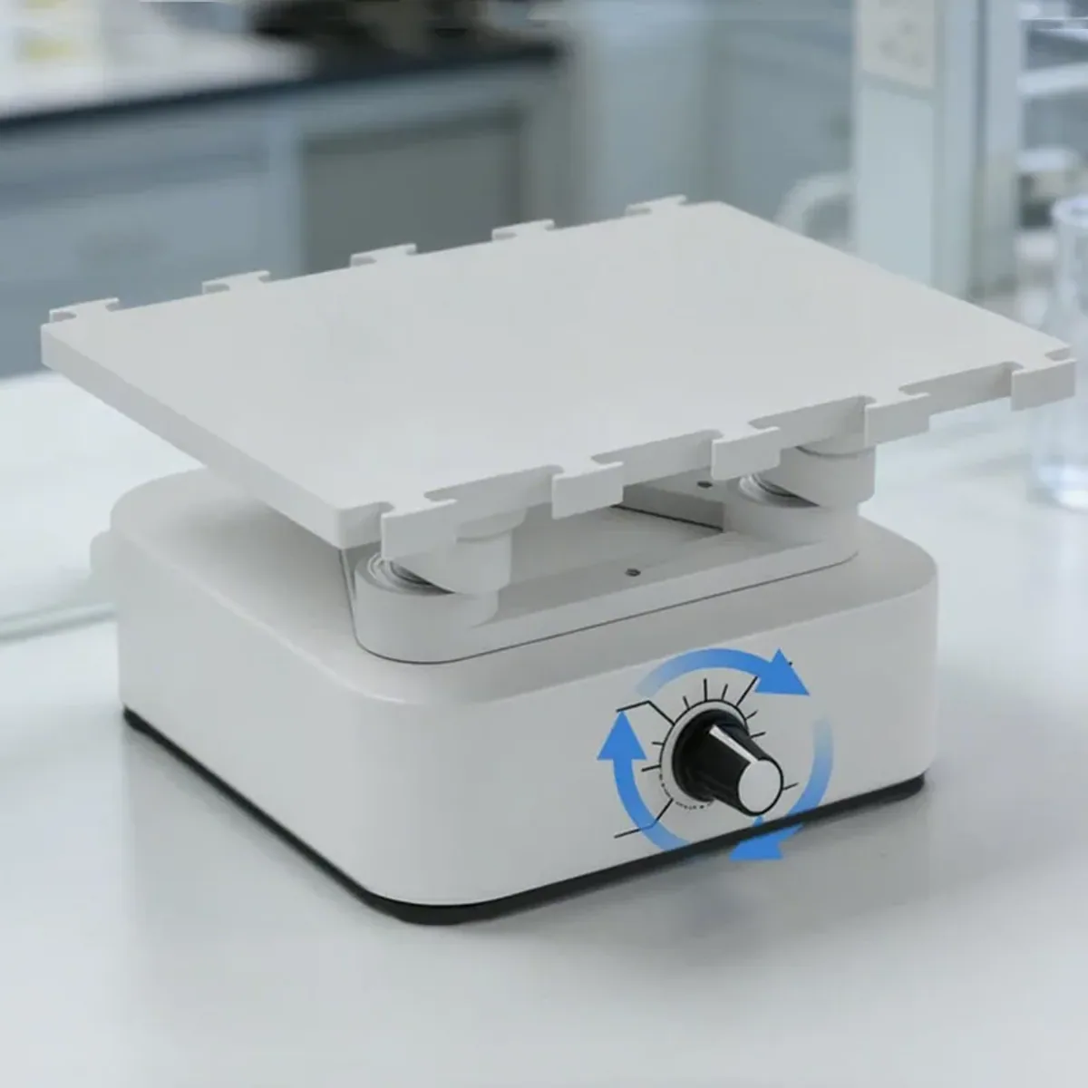White mini orbital shaker with a platform edged by raised tabs and a speed dial on the front of the base