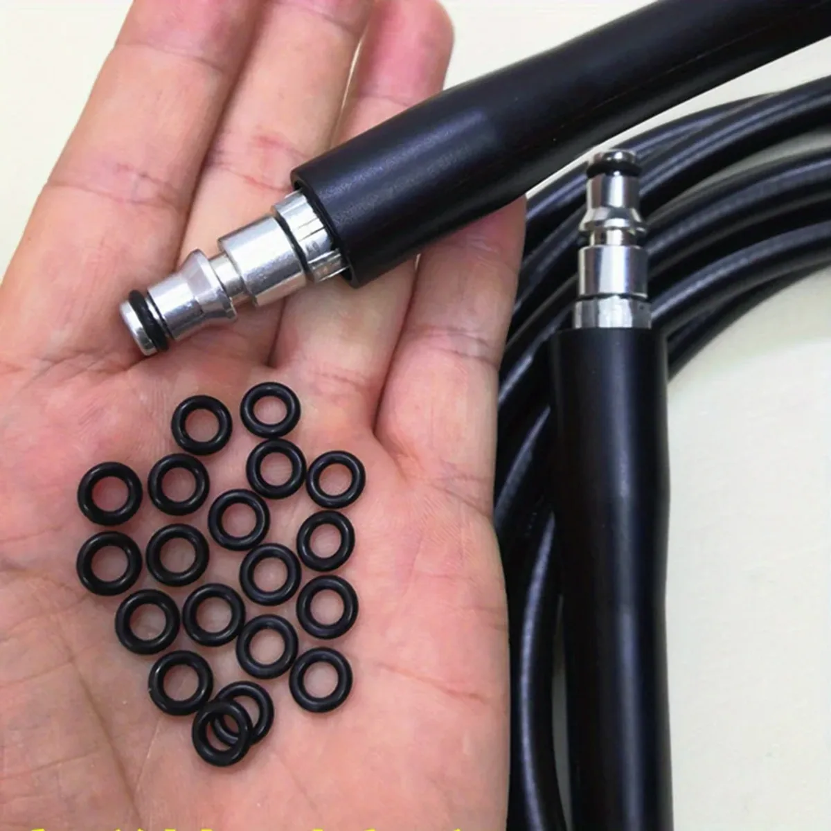 Hand holding pressure washer fittings and black rubber O-rings next to a hose
